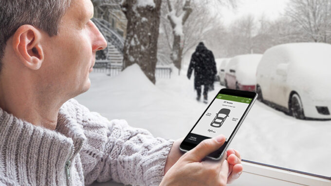A man looking at his phone with cars covered in snow in the background