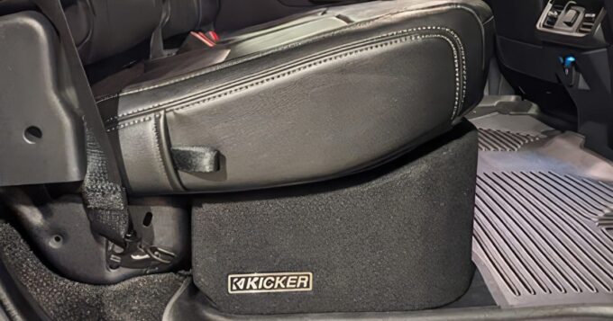 The passenger side seat of a vehicle with the kicker logo on an enclosure underneath it